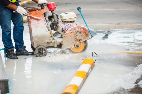 Worker guiding a walk-behind wet saw to cut a slot in concrete pavement during vehicle loop detector installation.