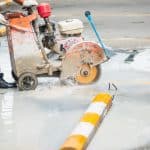 Worker guiding a walk-behind wet saw to cut a slot in concrete pavement during vehicle loop detector installation.