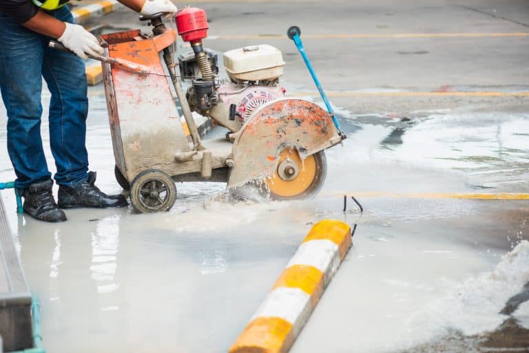 Worker guiding a walk-behind wet saw to cut a slot in concrete pavement during vehicle loop detector installation.