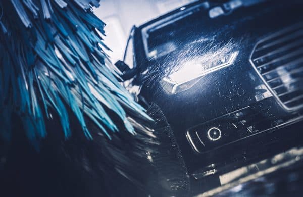 A sedan moving through spray and spinning brushes in a wash tunnel, the wet conditions car wash photo eyes have to work in.
