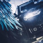 A sedan moving through spray and spinning brushes in a wash tunnel, the wet conditions car wash photo eyes have to work in.